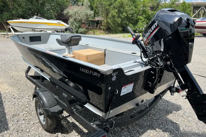 Slide: The Image of 2026 Lund 1600 Fury Tiller boat with Mercury engine on trailer, parked outdoors. - 12