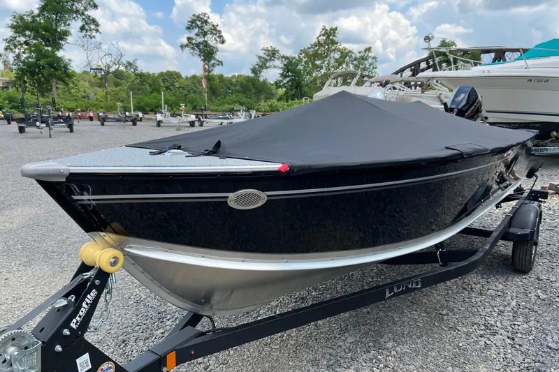 Slide: The Image of 2026 Lund 1600 Fury Tiller boat with cover on trailer, parked outdoors. - 2