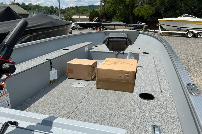 Slide: The Image of 2026 Lund 1600 Fury Tiller boat interior with boxes on deck, parked outdoors. - 9