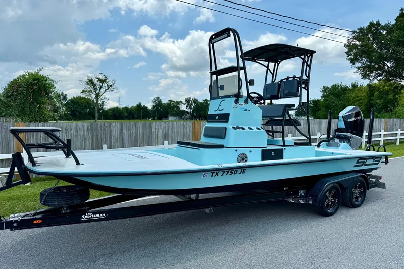Slide: The Image of 2020 SCB R24 boat on trailer, light blue, parked on street, clear sky background. - 1
