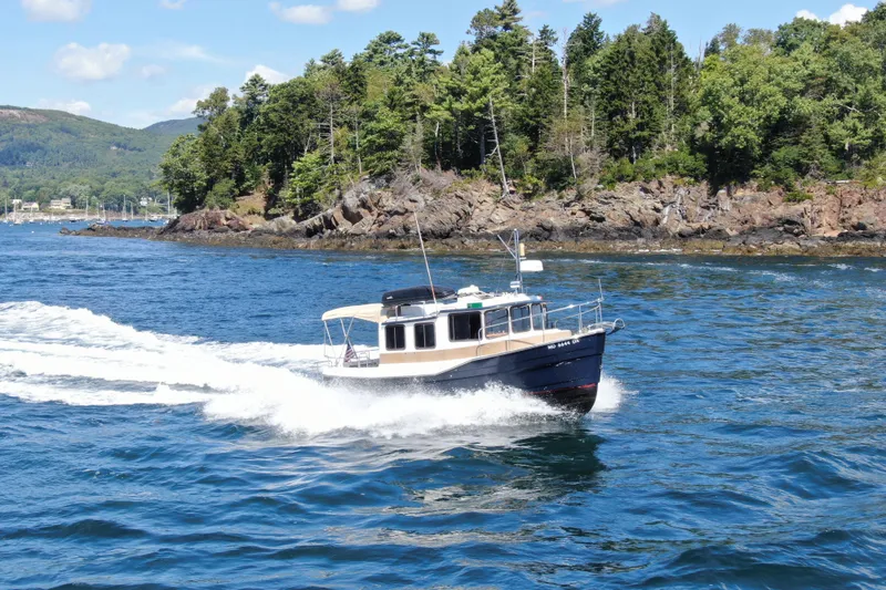 The Image of 2012 Ranger Tugs R-27 cruising on scenic blue waters near a rocky, forested shoreline. - 0