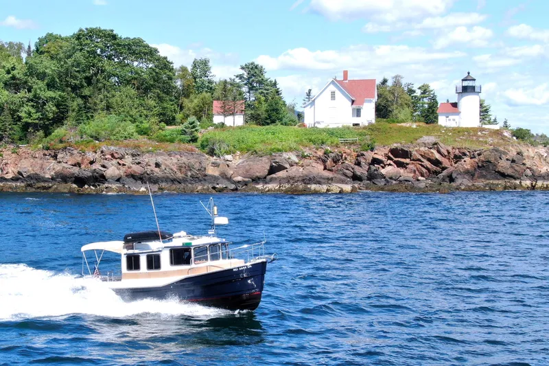 Slide: The Image of 2012 Ranger Tugs R-27 cruising near rocky shoreline with lighthouse and trees. - 95
