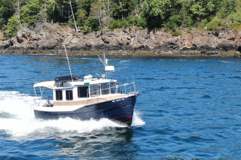 Slide: The Image of 2012 Ranger Tugs R-27 cruising on blue water near rocky shoreline. - 97