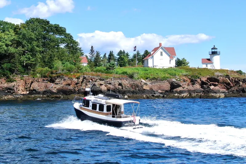Slide: The Image of 2012 Ranger Tugs R-27 cruising near a rocky shoreline with a lighthouse in the background. - 98