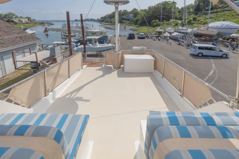 Slide: The Image of 1988 Grand Banks 36 Sedan deck view with striped seating, overlooking marina and parked vehicles. - 19