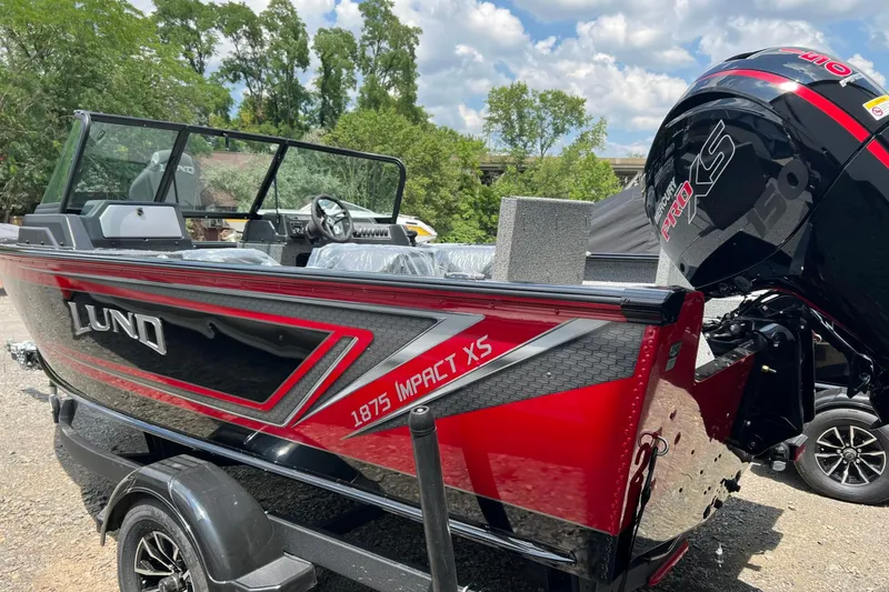 Slide: The Image of 2026 Lund 1875 Impact XS Sport boat with sleek red and black design, parked outdoors. - 18