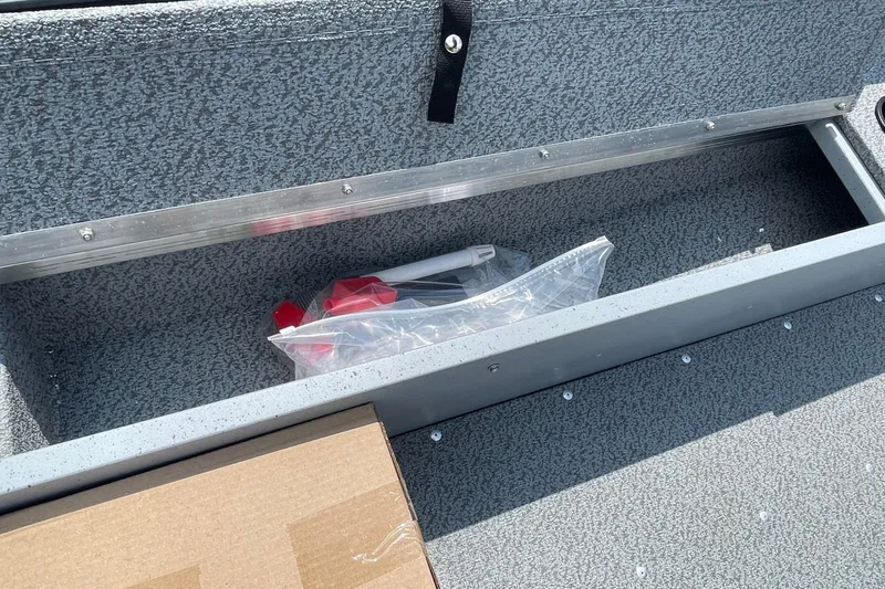 Slide: The Image of Storage compartment in a 2026 Lund 1600 Fury SS boat, containing a plastic bag and cardboard box. - 10