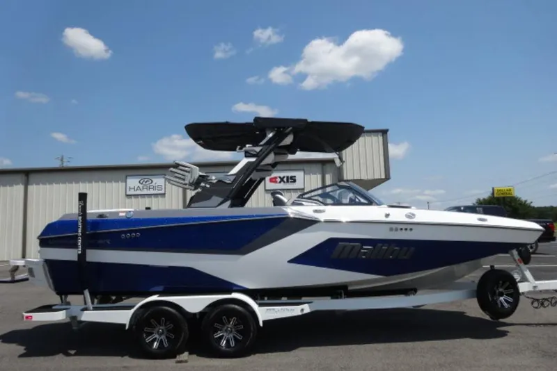 The Image of 2026 Malibu 23 MXZ boat on trailer, blue and white design, parked outdoors. - 0