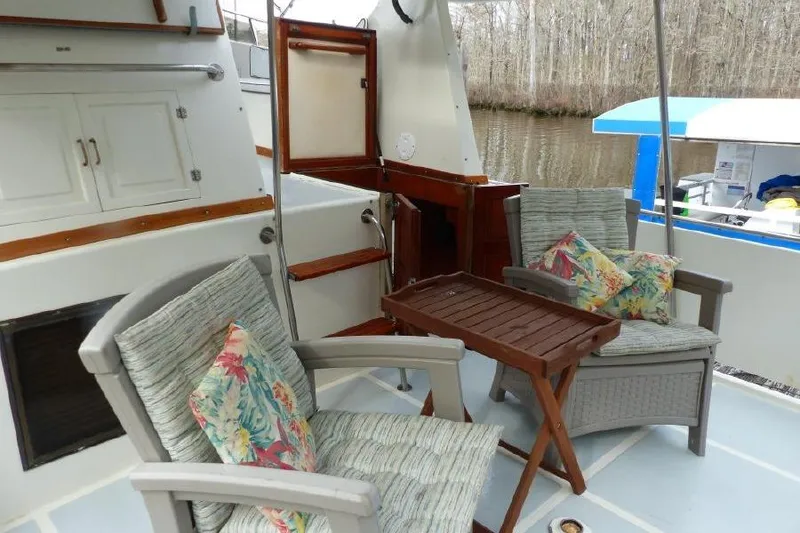Slide: The Image of 1987 Marine Trader Sundeck with cozy seating and table on deck, near a serene waterway. - 22