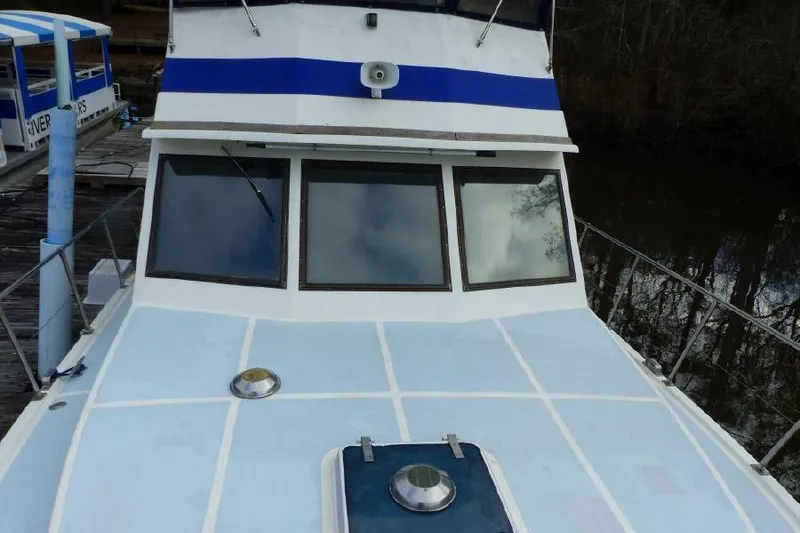 Slide: The Image of 1987 Marine Trader Sundeck boat with blue and white exterior, docked near wooded area. - 6