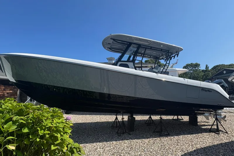 Slide: The Image of 2025 Edgewater 340CC boat with sleek design, docked near lush greenery under clear blue sky. - 3