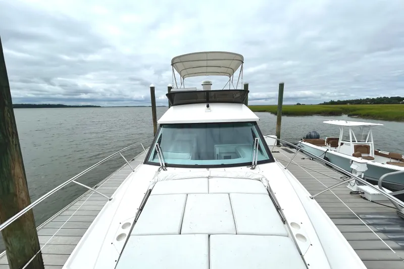 Slide: The Image of 2024 Regal 42 FXO yacht docked by a serene waterfront under cloudy skies. - 6