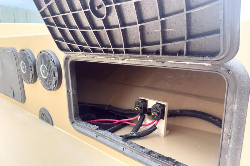 Slide: The Image of Open storage compartment on 2026 Carolina Skiff E21 DLX CC boat, showing wiring and speakers. - 27