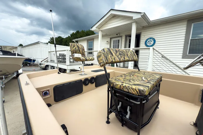 Slide: The Image of 2026 Carolina Skiff E21 DLX CC boat with camo seating, docked near a white building. - 8