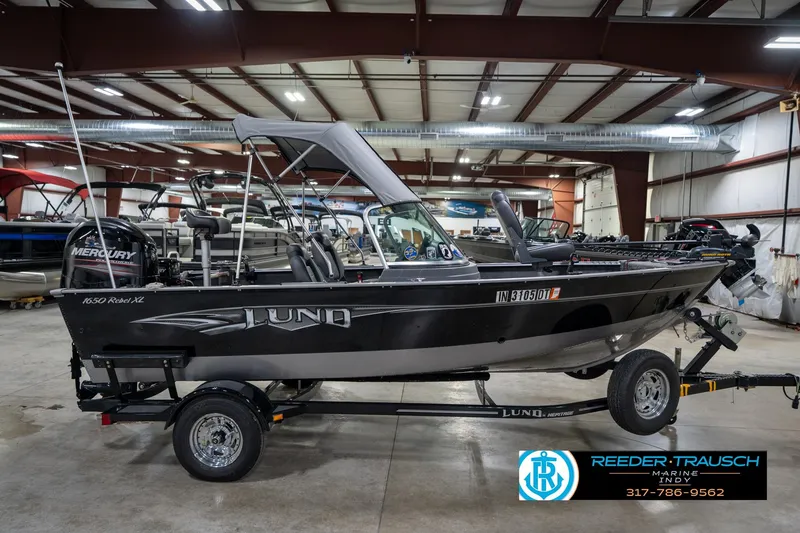 Slide: The Image of 2014 Lund 1650 Rebel XS boat in showroom, featuring Mercury engine and trailer. - 7