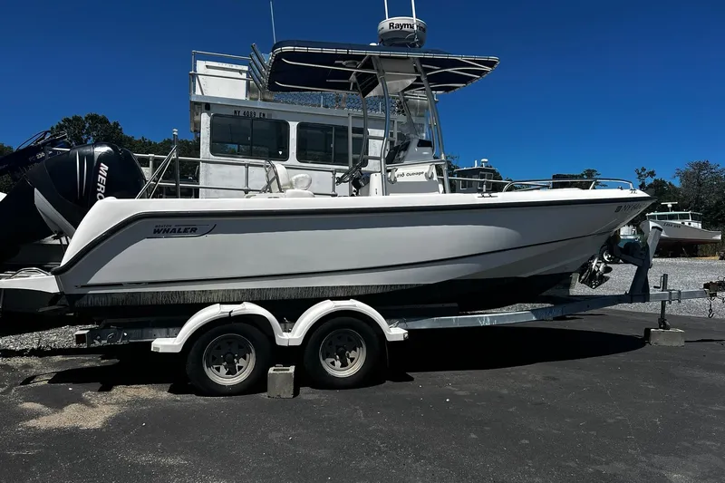 Slide: The Image of 2006 Boston Whaler 210 Outrage boat on trailer, parked outdoors under clear blue sky. - 0