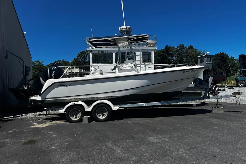 Slide: The Image of 2006 Boston Whaler 210 Outrage boat on trailer, parked outdoors under clear blue sky. - 1