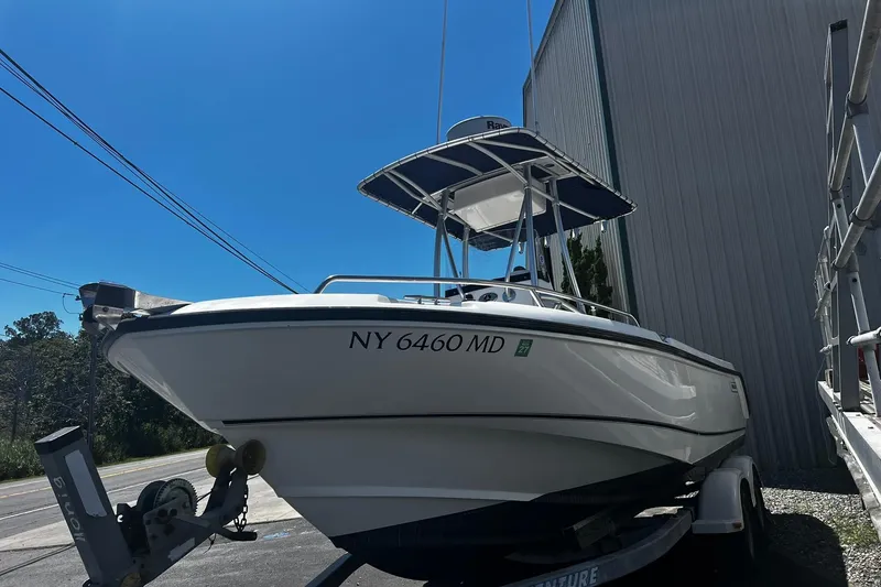 Slide: The Image of 2006 Boston Whaler 210 Outrage boat on trailer, parked outdoors under clear blue sky. - 2