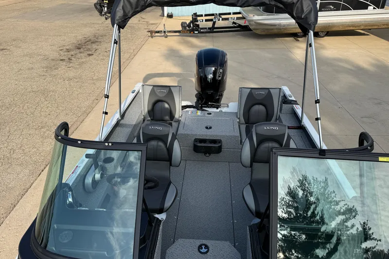 Slide: The Image of 2026 Lund 1675 Adventure Sport boat interior with seating and motor, docked on pavement. - 16