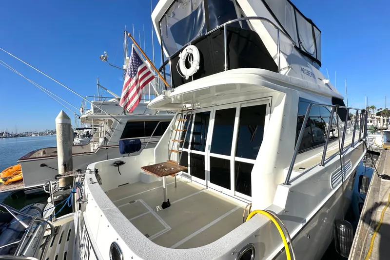 Slide: The Image of 2003 Ocean Alexander 42 Sport Sedan yacht docked at marina, featuring spacious deck and American flag. - 4
