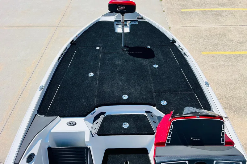 Slide: The Image of 2025 Ranger Z520 boat deck with black carpeting and red accents, parked on concrete. - 10