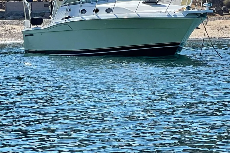 Slide: The Image of 2003 Wellcraft 330 Coastal boat anchored in calm blue waters near a sandy shore. - 20