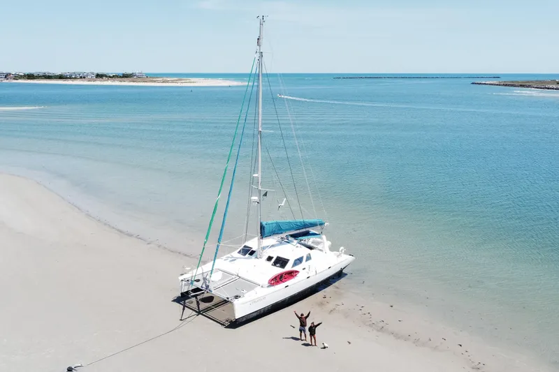 Slide: The Image of 2001 Voyage 440 catamaran beached on sandy shore with two people celebrating. - 0