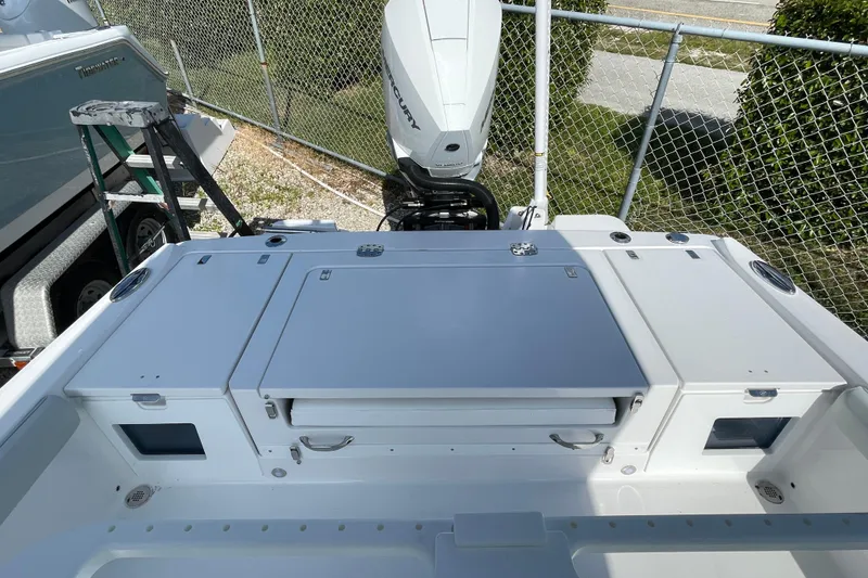 Slide: The Image of 2026 Blackfin 242HB boat deck with Mercury outboard motor, parked near a chain-link fence. - 26