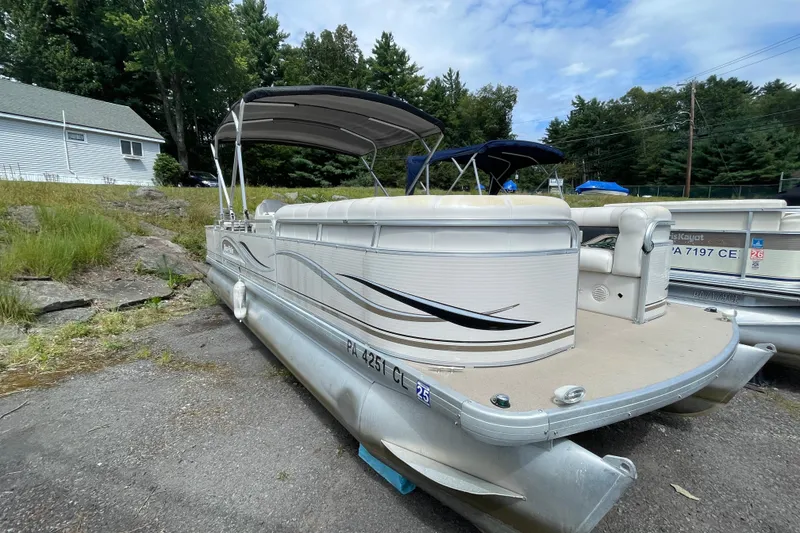 Slide: The Image of 2002 Godfrey Aqua Patio 2424DF pontoon boat parked on a paved surface, surrounded by trees. - 10