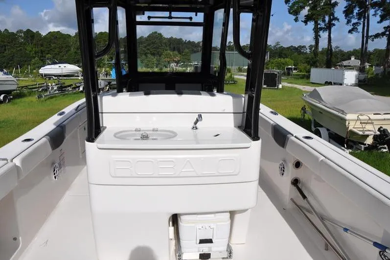 Slide: The Image of 2023 Robalo R272 Center Console boat interior with sink and storage, parked outdoors. - 7
