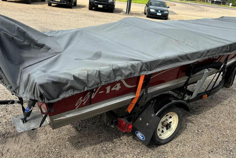 Slide: The Image of 1999 Lund SSV 14 Tiller boat covered on a trailer in a parking lot. - 10