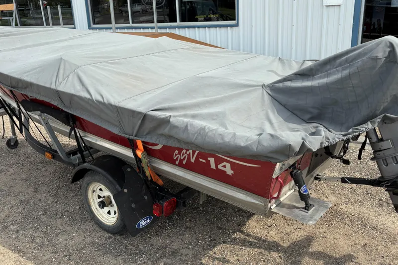 Slide: The Image of 1999 Lund SSV 14 Tiller boat covered on trailer, parked outside a building. - 11