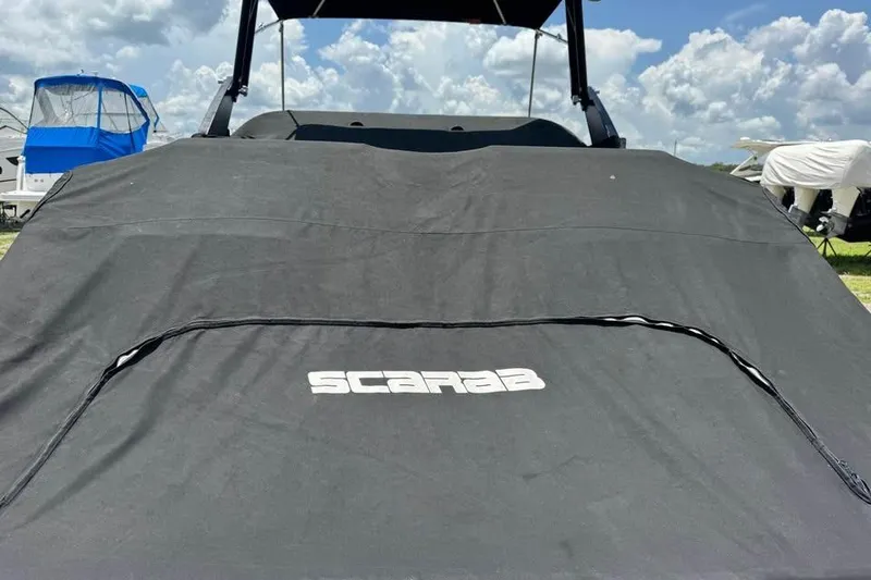 Slide: The Image of 2023 Scarab 255 ID boat with cover, under a partly cloudy sky. - 19