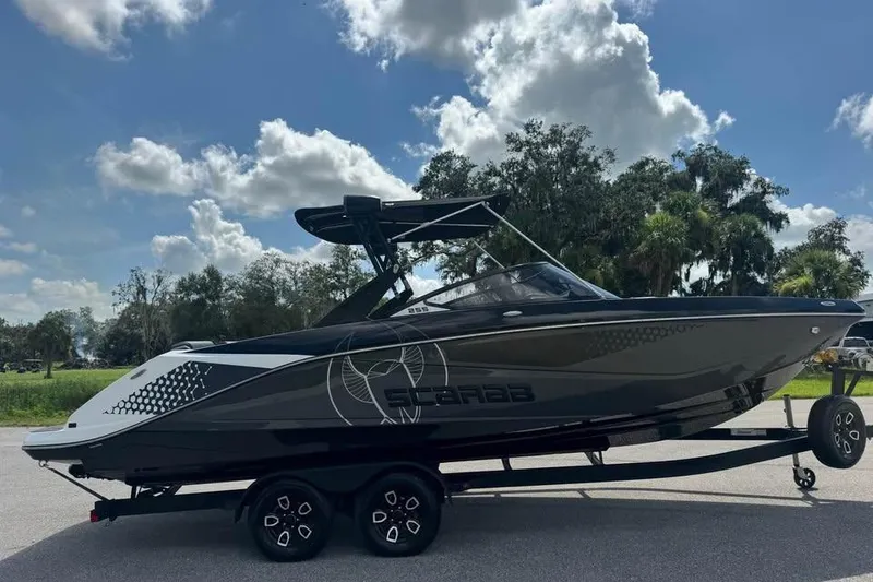 Slide: The Image of 2023 Scarab 255 ID boat on trailer under a blue sky with clouds. - 2