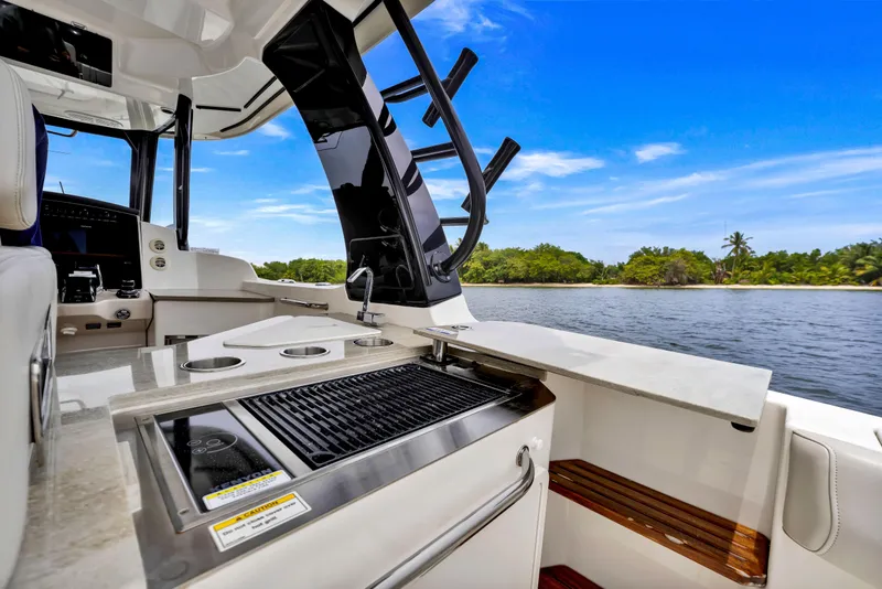 Slide: The Image of 2023 Boston Whaler 350 Realm boat interior with grill, ocean view, and tropical island backdrop. - 16