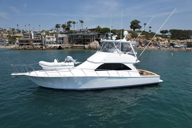 Slide: The Image of 2005 Viking 48 Convertible yacht on calm coastal waters, with scenic beachfront background. - 5