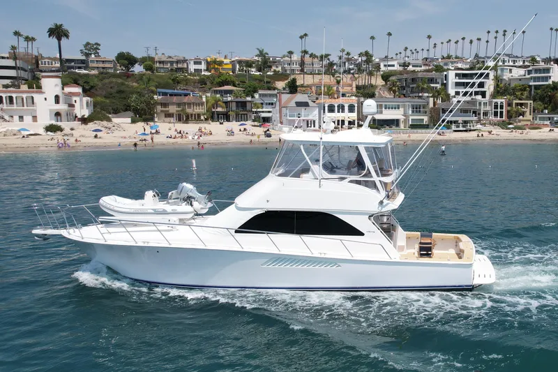 Slide: The Image of 2005 Viking 48 Convertible yacht cruising near a scenic beach with coastal homes. - 8