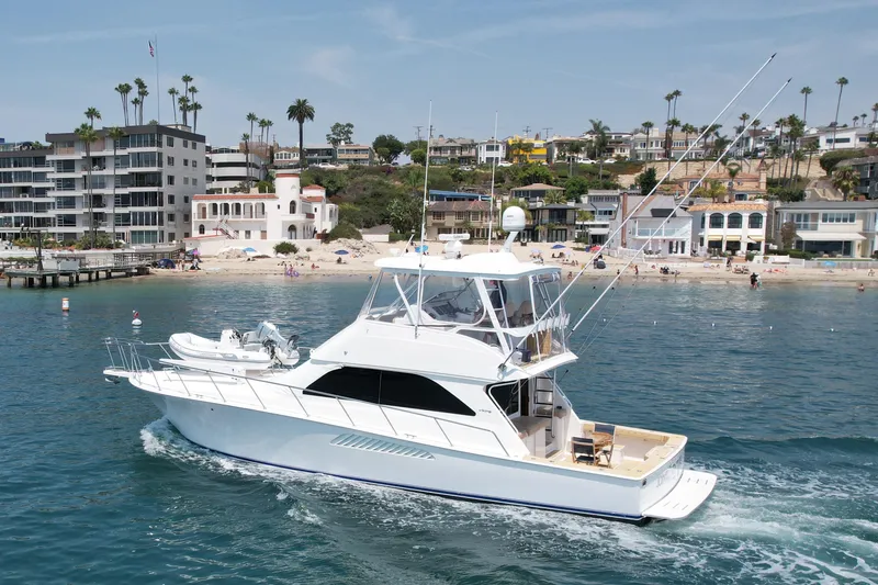 Slide: The Image of 2005 Viking 48 Convertible yacht cruising near a scenic beachfront with modern buildings. - 9