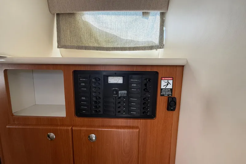 Slide: The Image of 2004 Bayliner 285 interior control panel with wooden cabinetry and warning label. - 12