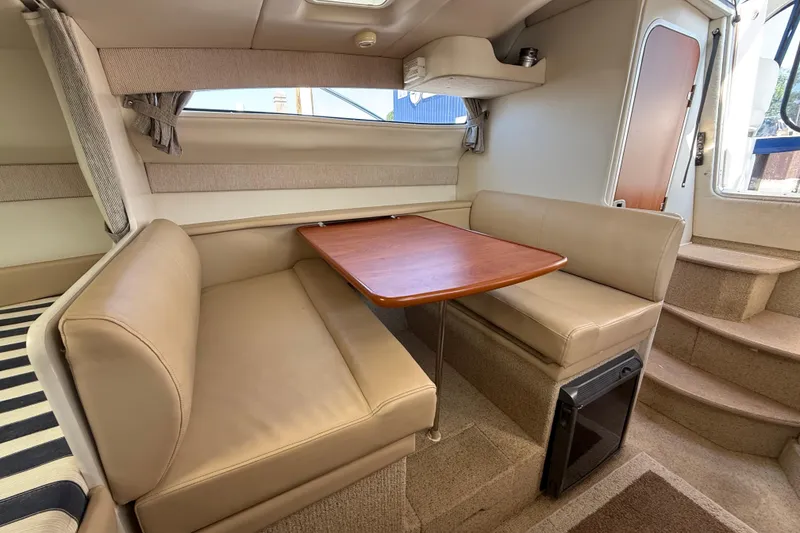 Slide: The Image of 2004 Bayliner 285 interior with beige seating, wooden table, and carpeted stairs. - 16