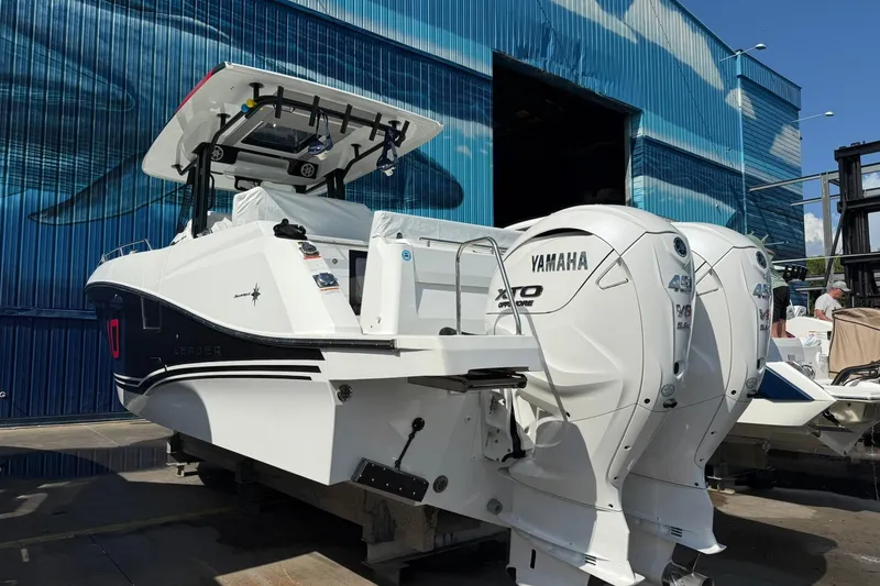 Slide: The Image of 2024 Jeanneau Leader 10.5 CC boat with twin Yamaha engines, docked near a blue warehouse. - 11