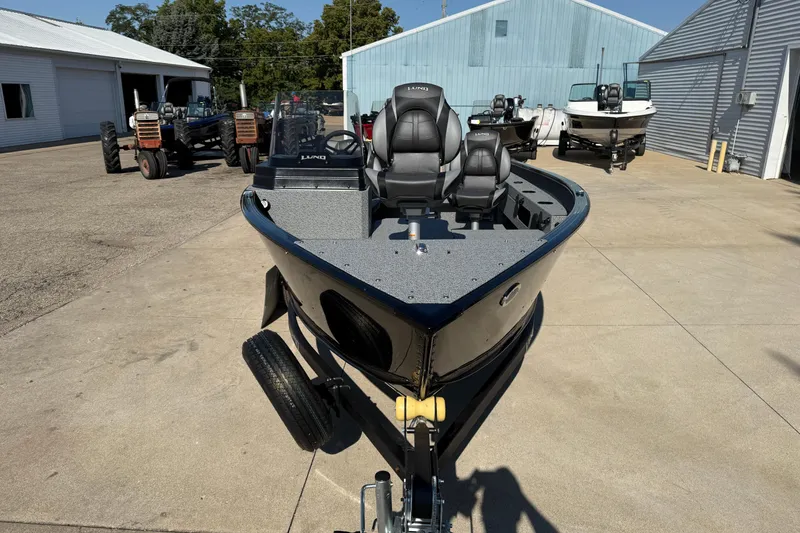 Slide: The Image of 2026 Lund 1675 Adventure SS boat on trailer, parked outdoors near tractors and buildings. - 3