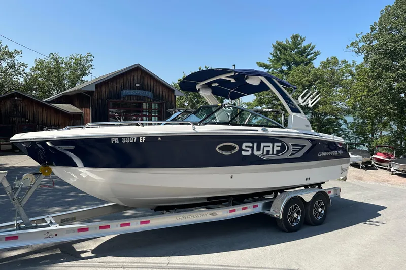 Slide: The Image of 2024 Chaparral 26 Surf boat on trailer, parked outdoors near rustic buildings. - 0