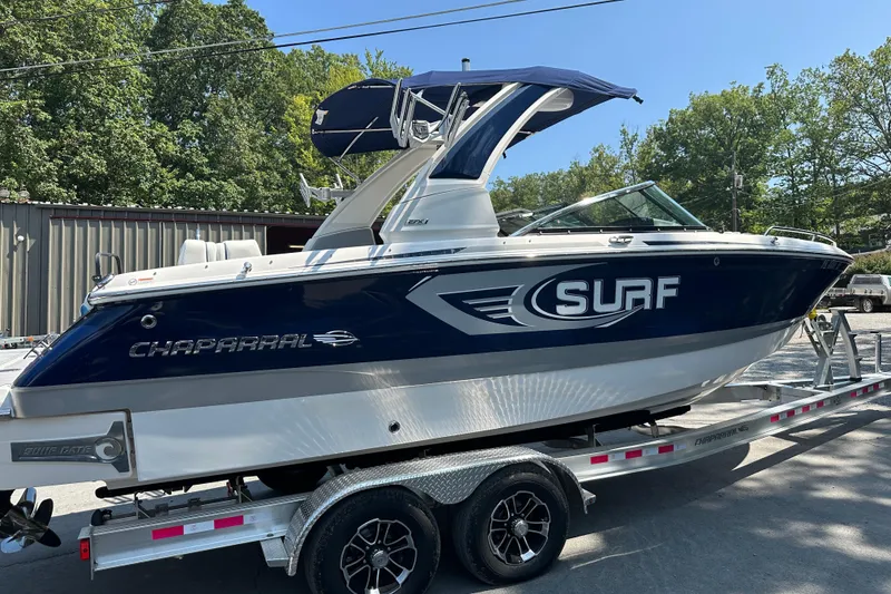Slide: The Image of 2024 Chaparral 26 Surf boat on trailer, blue and white design, parked outdoors. - 1