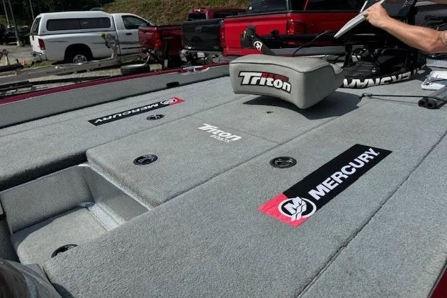 Slide: The Image of 2005 Triton Tr-186 DC boat deck with Mercury branding, featuring gray carpet and storage compartments. - 5