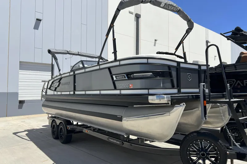 Slide: The Image of 2022 Godfrey AquaPatio 255 SBW pontoon boat on trailer, parked near a building. - 4