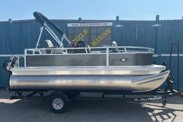 The Image of 2026 Sun Tracker Bass Buggy 16 XL Select pontoon boat on trailer, parked outdoors. - 0