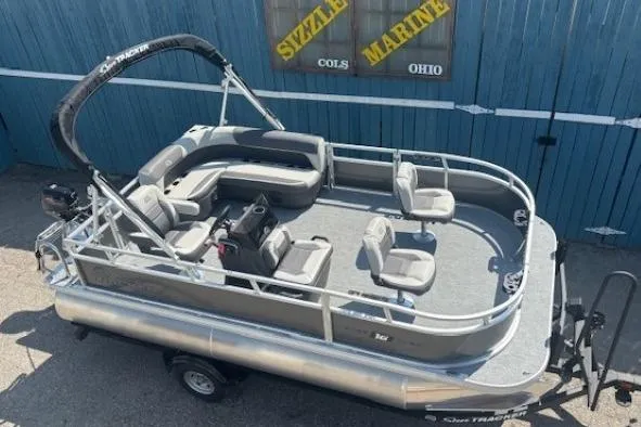 Slide: The Image of 2026 Sun Tracker Bass Buggy 16 XL Select pontoon boat on trailer, parked outside. - 7