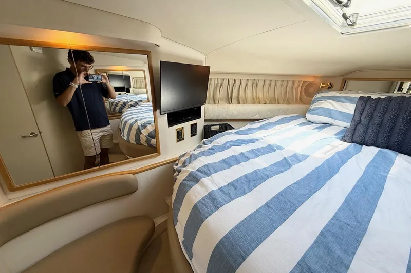 Slide: The Image of 1998 Sea Ray 400 Express Cruiser cabin with striped bedding and wall-mounted TV. - 21