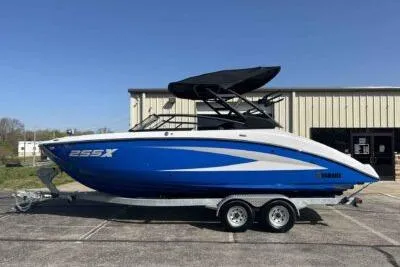 Slide: The Image of 2025 Yamaha Boats 255XD in blue on a trailer, parked outdoors. - 2